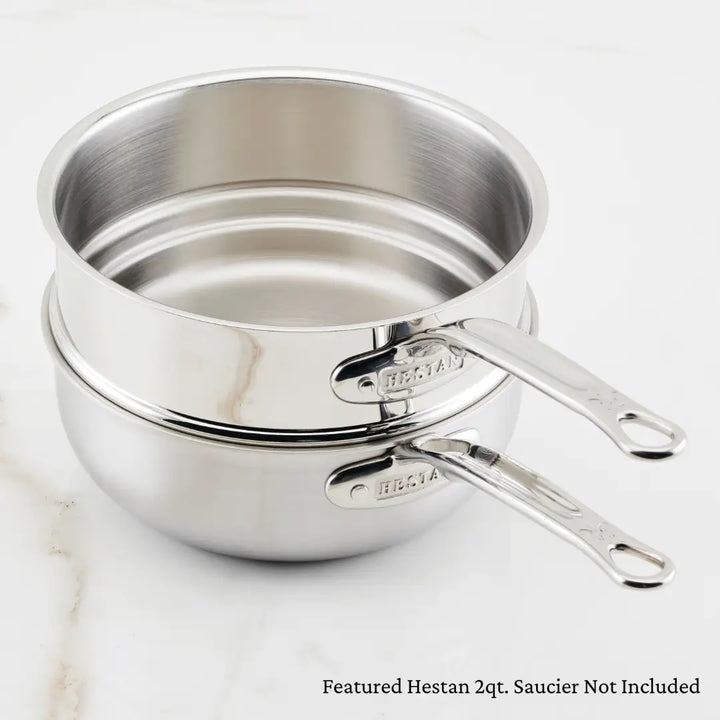 Two stacked stainless steel pans with clear handles feature the HESTAN brand, suggesting precise temperature control. Below, it states Featured Hestan Provisions Stainless Steel Double Boiler Insert, 3-Quart Not Included. The background is smooth and light-colored.