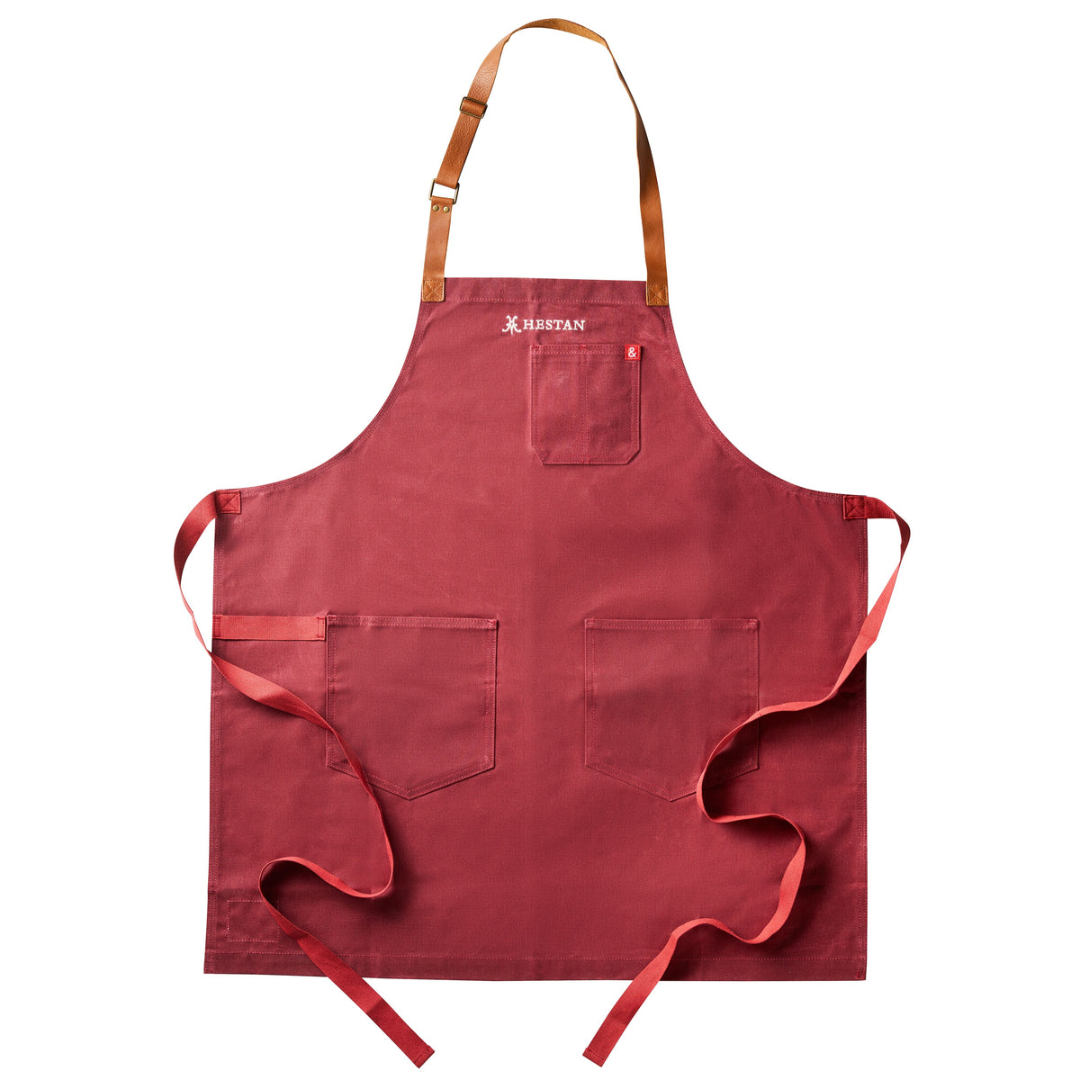 The Hestan x Hedley & Bennett Grilling Apron, a vibrant red piece from Accessories, features three front pockets and brown leather neck straps. Made of durable waxed canvas, it has a prominent logo at the top center for a sophisticated touch, set against a white background.