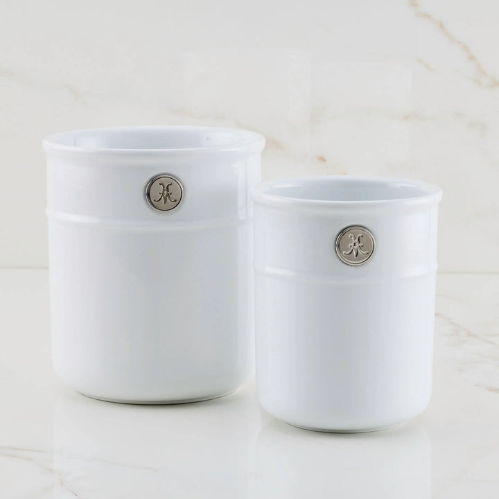 Two Hestan Provisions Porcelain Bain Maries, white with silver circular emblems and in different sizes, are placed side by side on a marble surface with a light beige background.