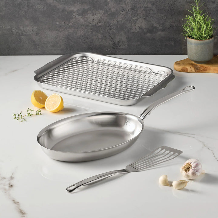 The Hestan Culinary Provisions Fish Pan Set, 4-Piece, is arranged on a white countertop with garlic, lemon halves, thyme, and a potted herb—an ideal seafood bakeware set for your kitchen.