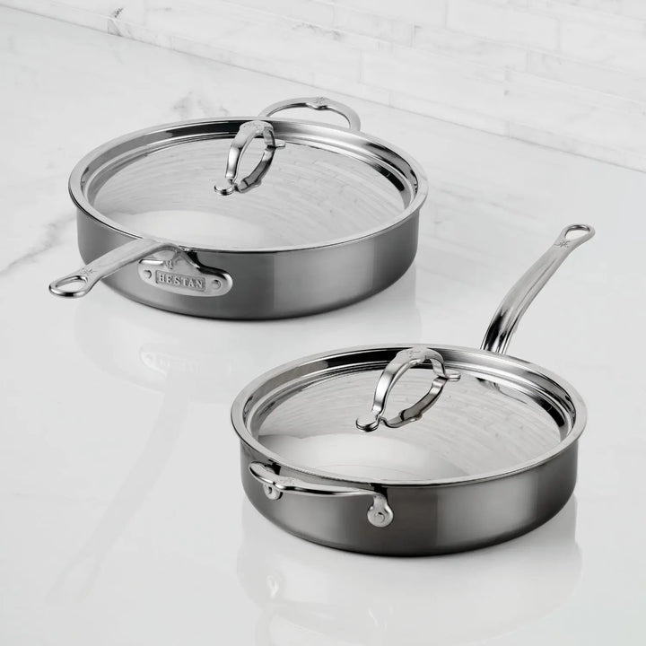 Two NanoBond Titanium Sauté Pans with lids sit on a white countertop. Featuring long handles, a polished finish, and the “NanoBond” brand, these stainless steel pans showcase advanced titanium cookware.