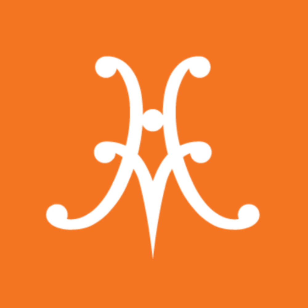 A white M monogram with curled ends on an orange background symbolizes VIP exclusivity at the Hestan Chefs Table™, presented by Inveterate.