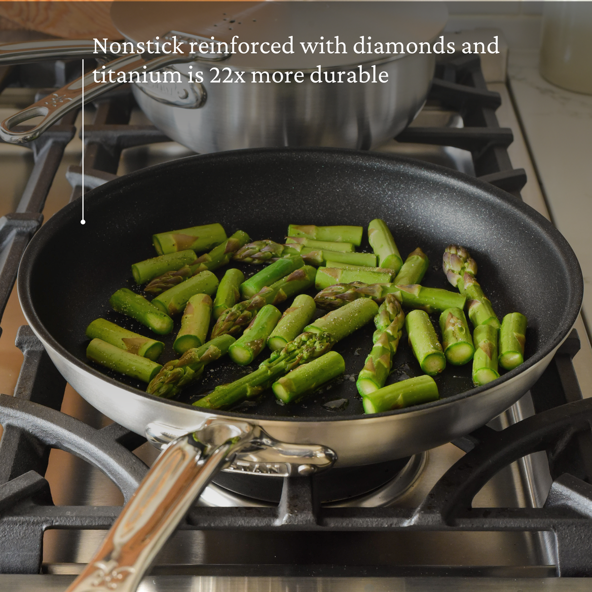 A Thomas Keller Commercial Clad Stainless Steel 7-Piece Cookware Set pan cooks asparagus on a gas stove, with a caption above: Nonstick reinforced with diamonds and titanium is 22x more durable.