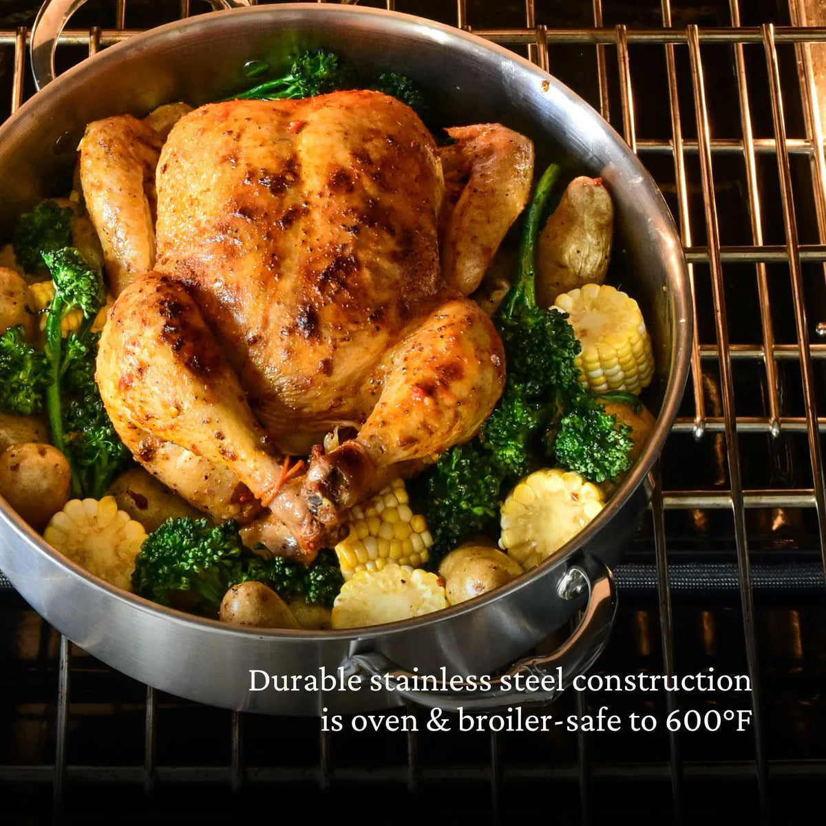 A whole roasted chicken rests in a Thomas Keller Commercial Clad Stainless Steel 11-Piece Cookware Set pan, surrounded by broccoli, corn, and potatoes. Text reads: Durable stainless steel is oven & broiler-safe to 600°F.