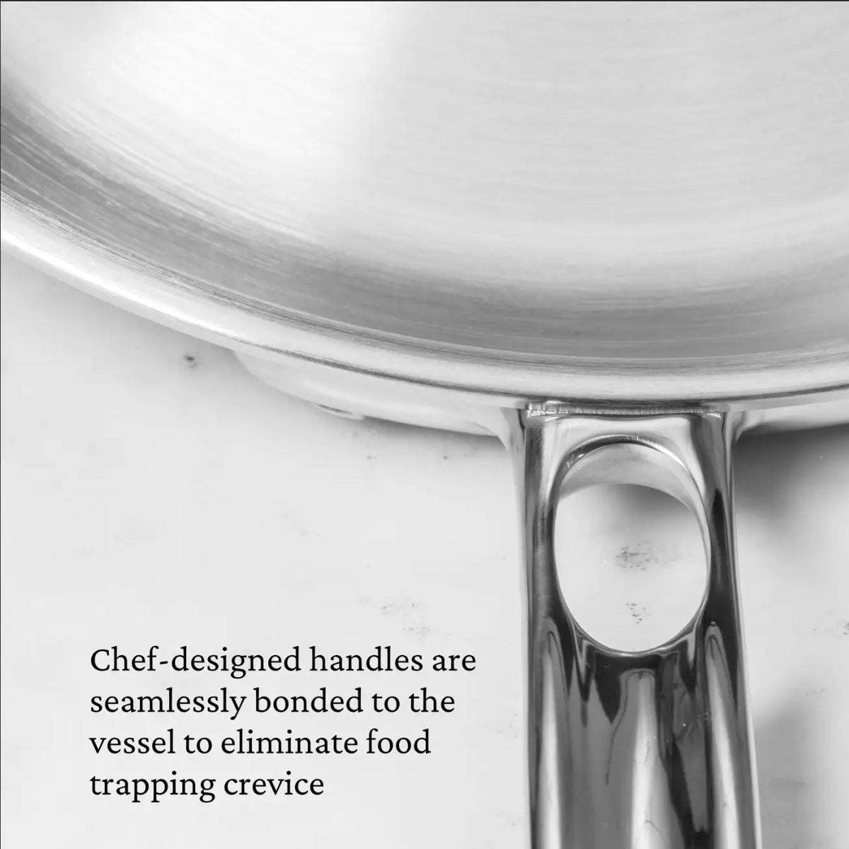 A close-up of the Thomas Keller Commercial Clad Stainless Steel 29-Piece Cookware Set shows seamlessly bonded chef-designed handles, eliminating crevices that trap food.