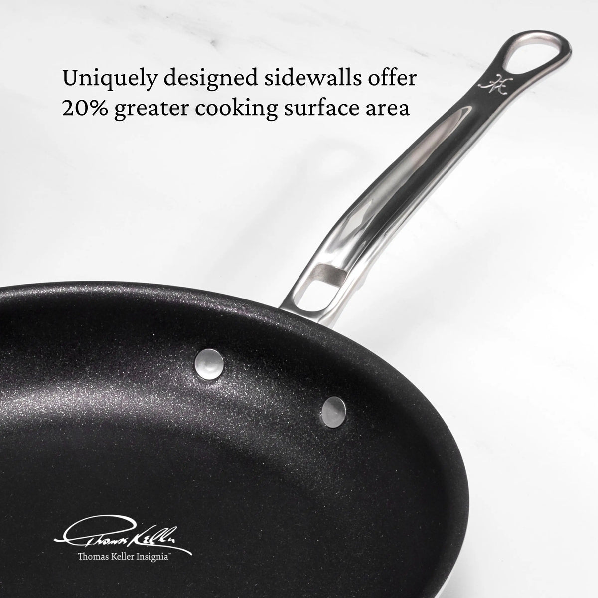 A Thomas Keller Commercial Clad Commercial Clad Stainless Steel 29-Piece Cookware Set frying pan sits on a white surface, featuring sidewalls for 20% more cooking space. Chef Thomas Keller’s signature is displayed at the bottom left corner.
