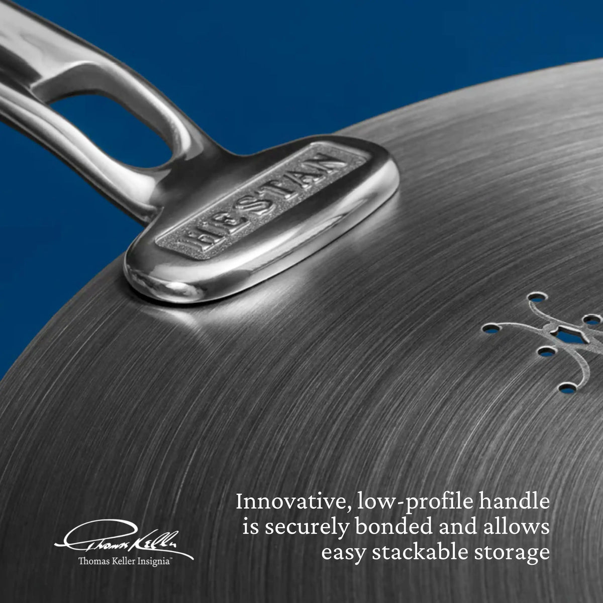 Close-up of a metal pan from the Thomas Keller Commercial Clad Stainless Steel 29-Piece Cookware Set, featuring an engraved signature, low-profile handle, and stackable design against a blue background.