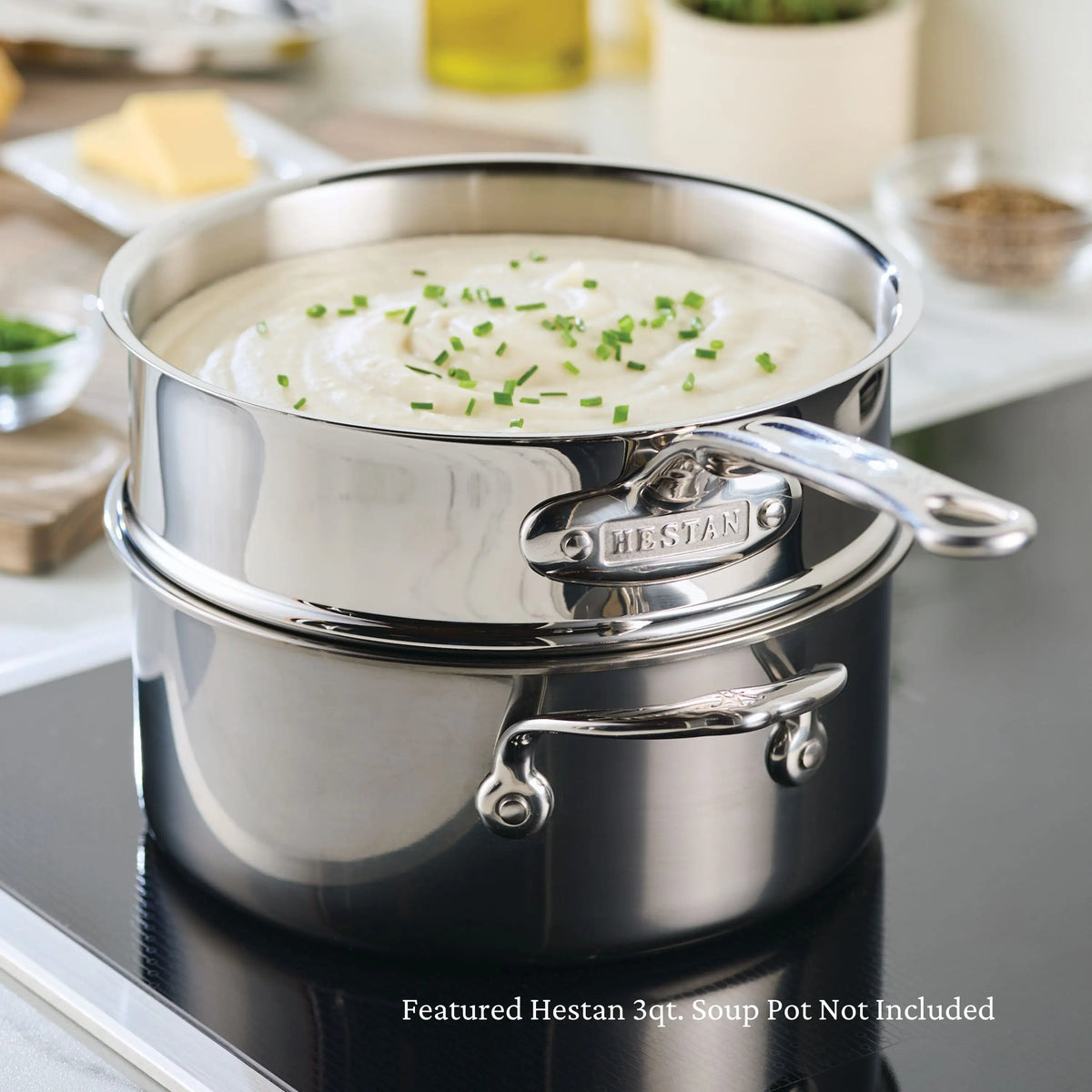 A creamy soup garnished with chives sits in a shiny pot from the Thomas Keller Commercial Clad Stainless Steel 29-Piece Cookware Set on an induction cooktop. Text: Featured item from set. Pot not included.