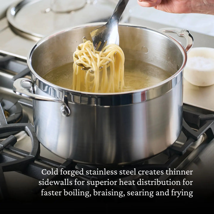 A hand lifts spaghetti with a fork from a pot on the stove. The ProBond Professional Clad Performance 28-piece Set ensures excellent heat distribution with its innovative tri-ply aluminum core, delivering perfectly cooked meals every time.