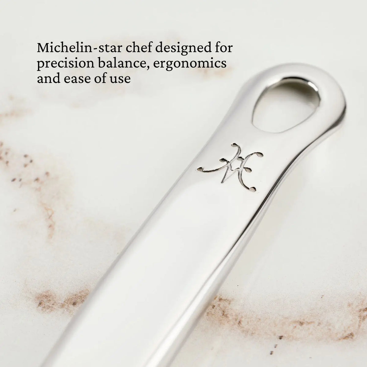 Close-up of Hestan Provisions OvenBond Tri-ply Epicurean Stainless Steel utensil handle, featuring a hanging hole and decorative marking. Designed by Michelin-star chef for precision balance, ergonomics, and ease of use.