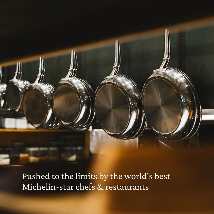 A row of shiny NanoBond Titanium Skillets hangs upside down. A kitchen setting forms the background, and text reads, Pushed to the limits by the world’s best Michelin-star chefs & restaurants.