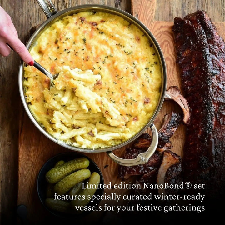 A hand serves macaroni and cheese from a round dish on a wooden board, with ribs and pickles nearby. Text reads: NanoBonds 10-piece Limited Edition Winter Titanium Cookware Set features specially curated vessels for your festive gatherings.