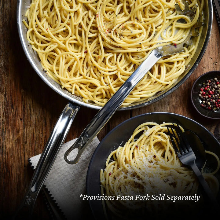 A NanoBond 10-piece Limited Edition Winter Titanium Cookware Set skillet holds spaghetti on a wooden table; beside it is a black bowl filled with more spaghetti. A stainless steel pasta fork rests in the skillet. A small bowl of peppercorns is nearby. Text reads: *Provisions Pasta Fork Sold Separately.