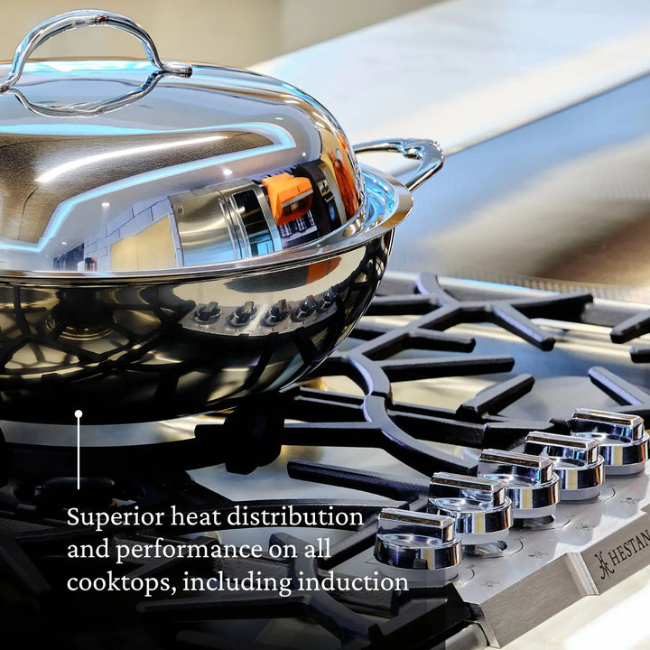 A close-up of the 10-piece Limited Edition Winter Titanium Cookware Set by NanoBond on a gas stove. The stovetop has multiple control knobs. Text reads, Superior heat distribution and performance on all cooktops, including induction.