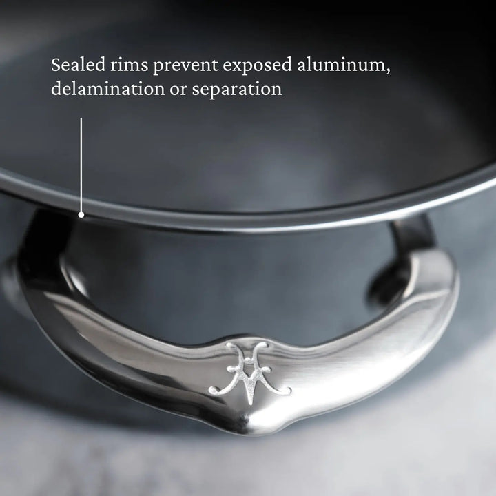 Close-up of a metal pot with a focus on the handle, featuring an engraved logo. The NanoBond 10-piece Limited Edition Winter Titanium Cookware Set includes sealed rims to prevent exposed aluminum, delamination, or separation.