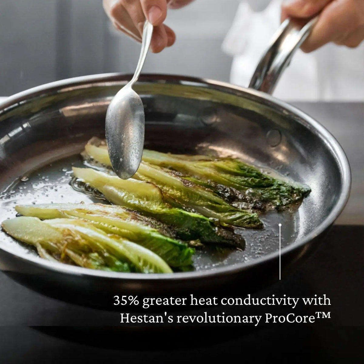 A hand holds a spoon above a stainless steel pan, basting several pieces of cooked lettuce. Text at the bottom highlights NanoBond®’s Titanium x Tyler Florence Cookware Set, 41-Piece, emphasizing its advanced Molecular Titanium technology and 35% greater heat conductivity with ProCore™ for exceptional performance.