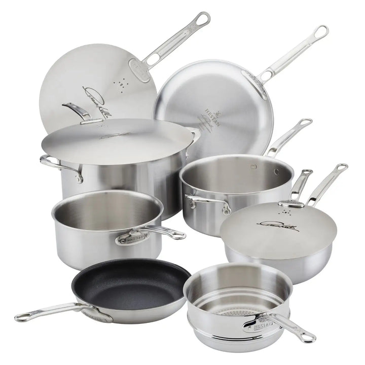 The Thomas Keller Insignia Commercial Clad Stainless Steel 10-Piece Cookware Set includes pots, pans, and lids. Some pans feature ProCore™ aluminum handles, and one has a non-stick surface, showcasing various sizes and types.