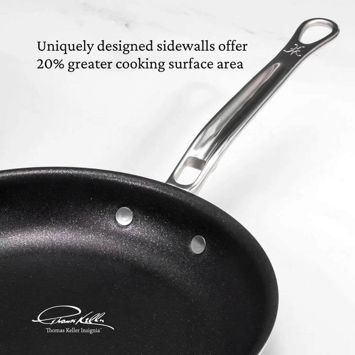 A black frying pan with a metal handle is shown on a white background, featuring the text: Uniquely designed sidewalls offer 20% more cooking surface area. Made with ProCore™ aluminum, it bears the signature: Thomas Keller Insignia.

.