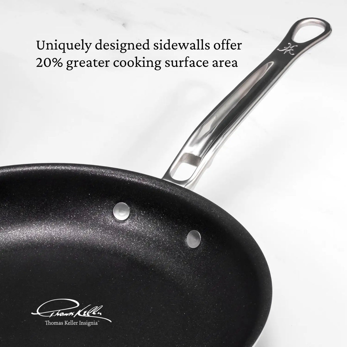 A close-up of a black nonstick frying pan from the Thomas Keller Commercial Clad Stainless Steel 10-Piece Cookware Set shows its metal handle and deep sidewalls, offering 20% more cooking surface. Signature and logo are displayed below.