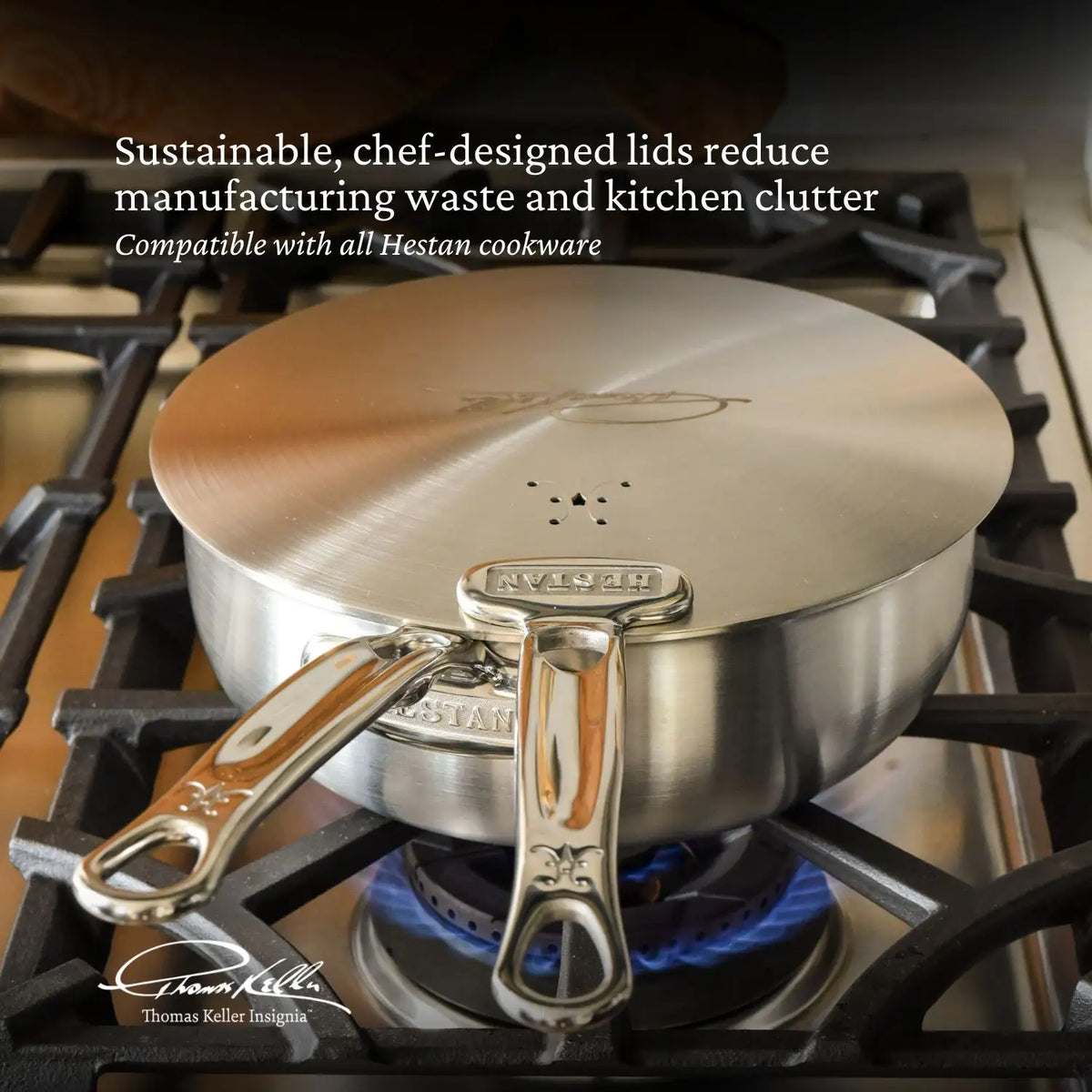 A Thomas Keller Commercial Clad pot from the Commercial Clad Stainless Steel 10-Piece Cookware Set rests on a gas stove with blue flames. Its vented lid is chef-designed for sustainability and fits other Thomas Keller cookware.