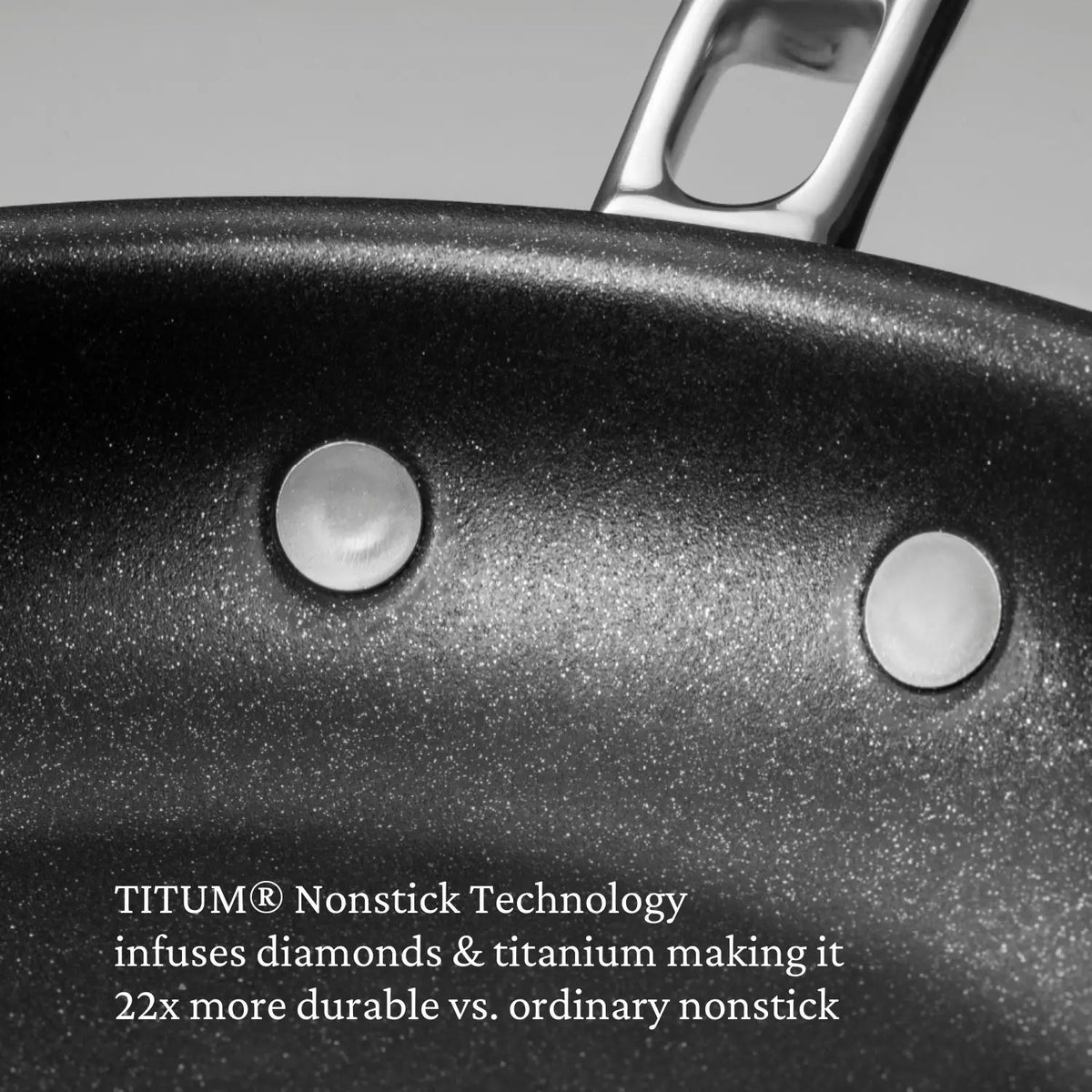 Close-up of a nonstick frying pan with two metal rivets and a handle. Text on the image reads: “Thomas Keller Commercial Clad TITUM® Nonstick Technology—22x more durable than ordinary stainless steel cookware.”.