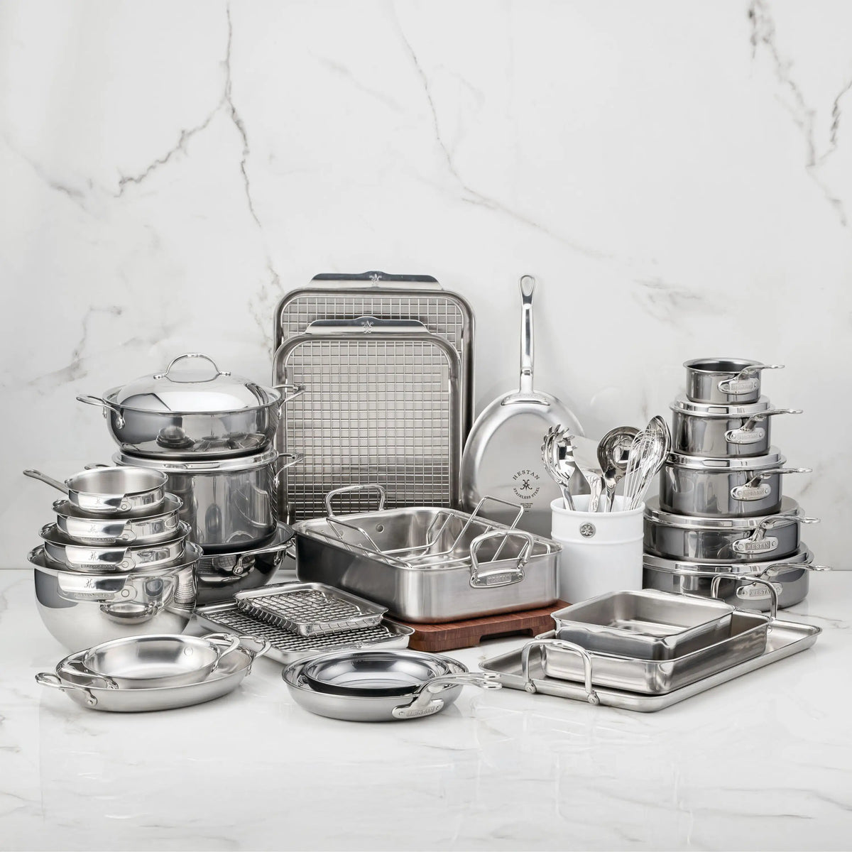 A large assortment of NanoBond® cookware, bakeware, and utensils is arranged on a white marble surface with a marble background. Items include pots, pans, trays, bowls, lids, ladles, and baking racks from the exceptional Titanium x Tyler Florence Cookware Set, 41-Piece collection by NanoBond®, designed for superior durability and performance.