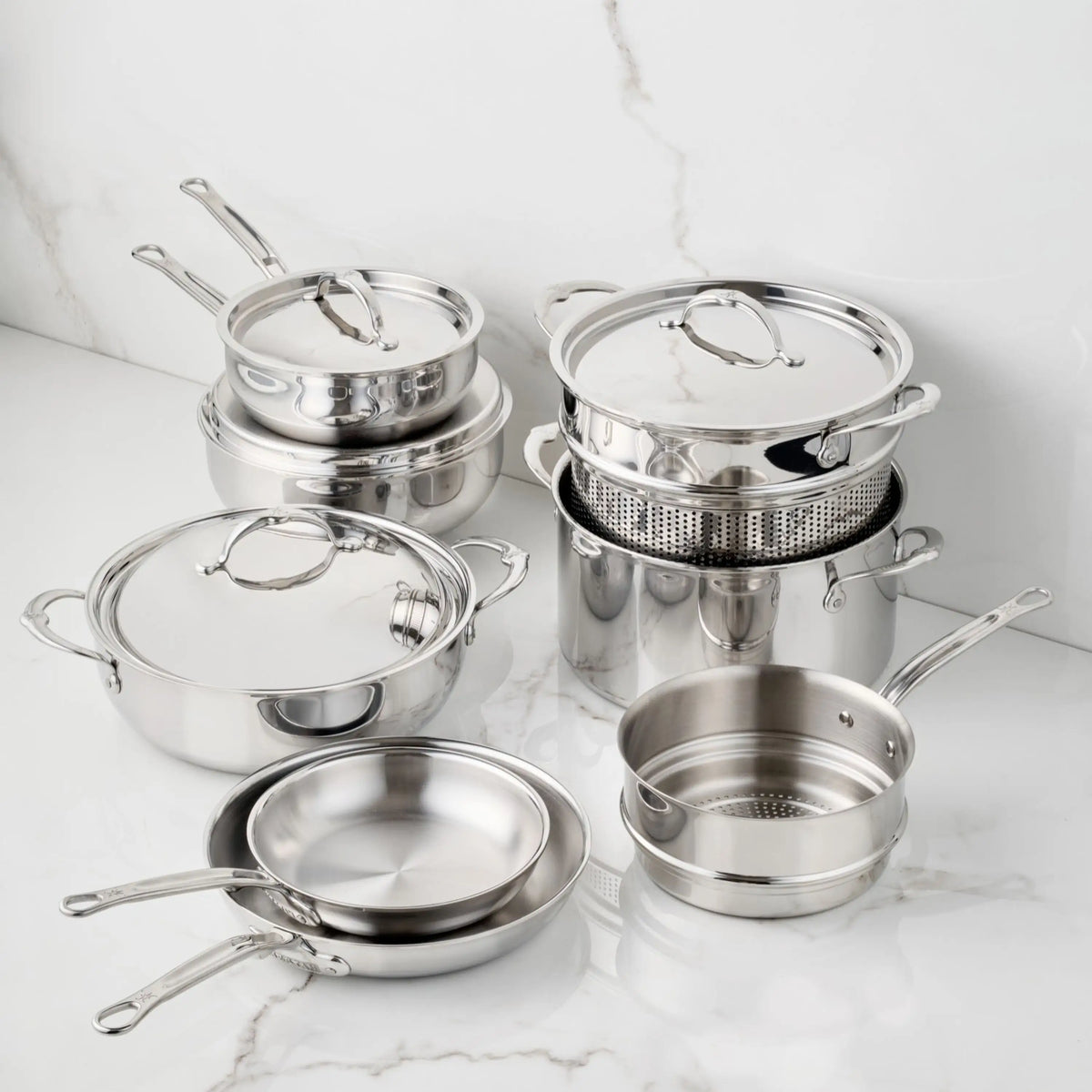 A 12-Piece Polished Clad Stainless Steel Set from ProBond Luxe® including various pots, pans, lids, and a steamer insert arranged on a marble surface.