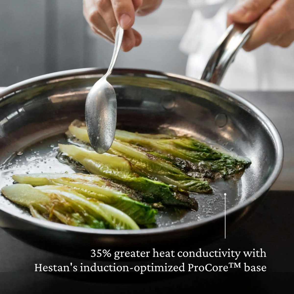 A hand holds a spoon over a stainless skillet searing romaine lettuce. Text below states, NanoBond Titanium Skillets offer 35% greater heat conductivity with an induction-optimized ProCore™ base and nonreactive titanium build.
