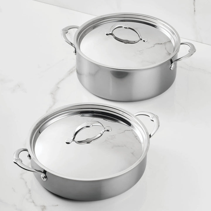 Two NanoBond Titanium Rondeaus with lids and handles are set on a white marble surface. The reflective cookware is positioned slightly apart, one rondeau in the foreground and one in the background.