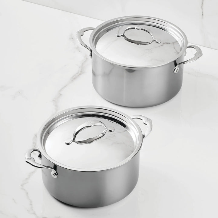 Two Titanium Stockpots from NanoBond, each with two side handles and topped with matching lids that have large looped handles, are displayed on a white marble surface.