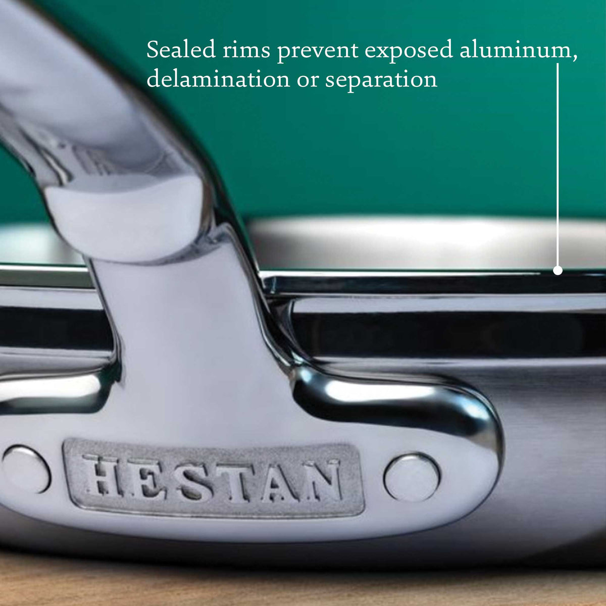 A close-up of a ProBond Professional Clad cookware handle with HESTAN engraved on it against a blurred green background. Text reads, Sealed rims prevent exposed aluminum, delamination, or separation, showcasing the superior quality of the 15-piece Professional Clad Stainless Steel Epicurean Set.