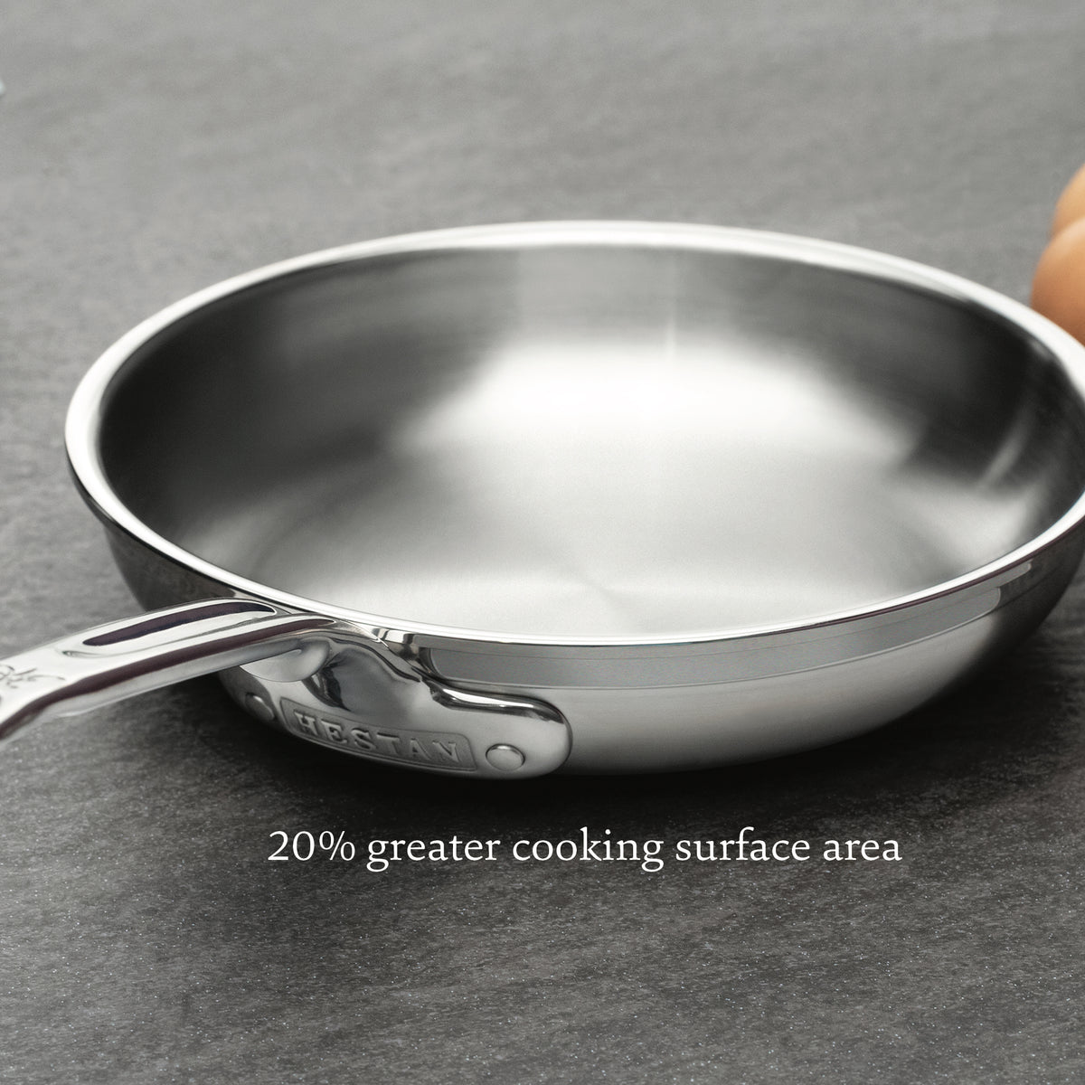 A close-up of a Professional Clad Stainless Steel Induction 4pc Cookware frying pan on a dark surface, showcasing its shiny, smooth finish. Text overlay reads 20% greater cooking surface area. Brand: ProBond.