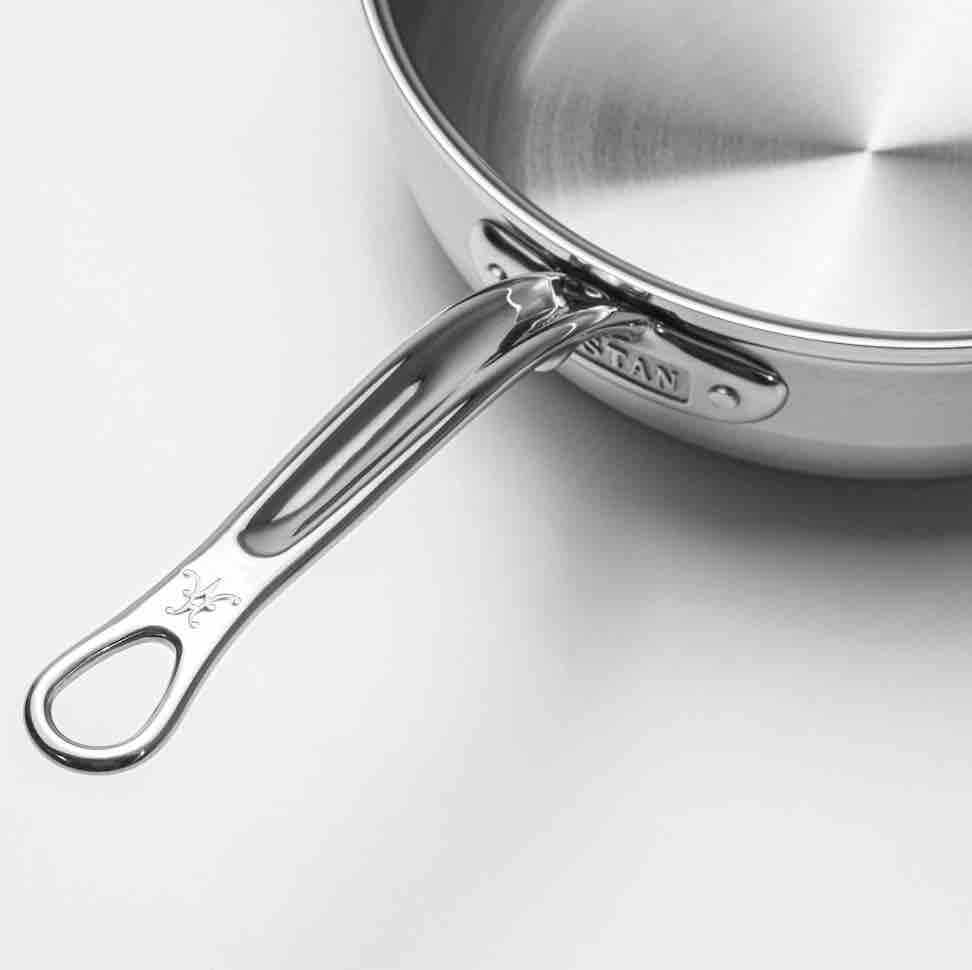 A close-up of a ProBond Professional Clad Stainless Steel Induction Cookware pan shows a polished metal handle with an engraved logo and oval hole, resting on a white surface. The tri-ply stainless steel design features a brushed interior finish.