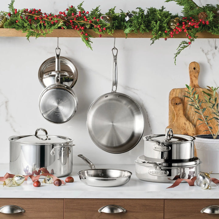 The ProBond® Luxe™ Polished Clad Stainless Steel Ultimate Set, 10-Piece, is displayed on a kitchen counter and hanging from hooks. Holiday greenery, red berries, cutting boards, and ornaments decorate the area above.