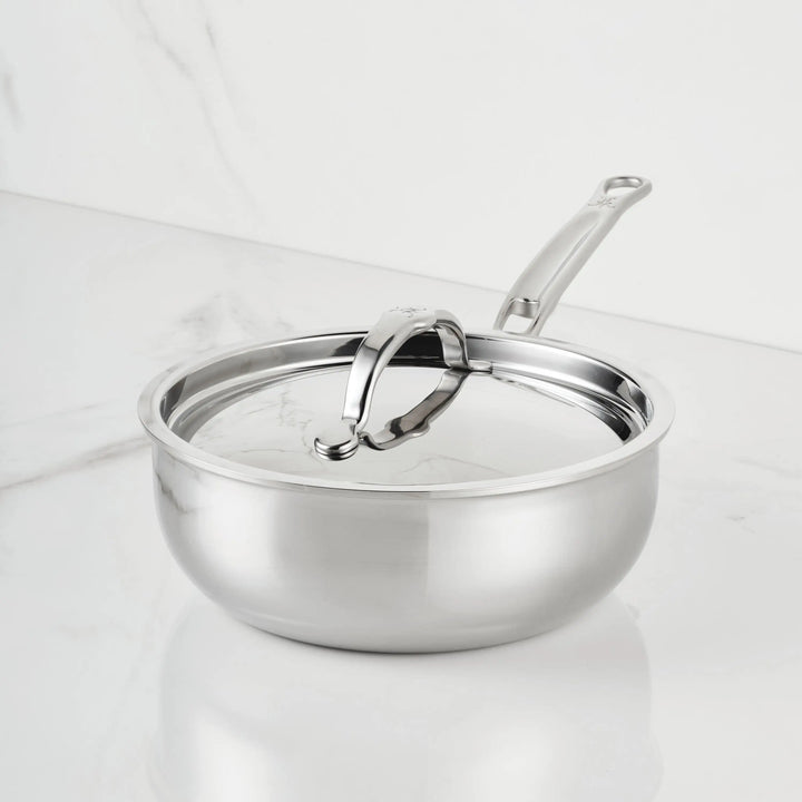 The ProBond® Luxe™ Polished Clad Stainless Steel Saucier Pan, 2-Quart, with lid and long ergonomic handle, sits on a white marble countertop, highlighting its durability and stylish design.