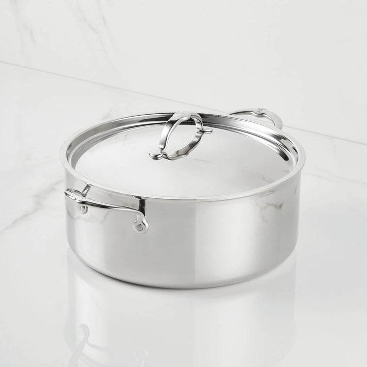 A ProBond® Luxe™ Polished Clad Stainless Steel Rondeau with metal handles and a lid is set on a white marble surface against a matching marble background.