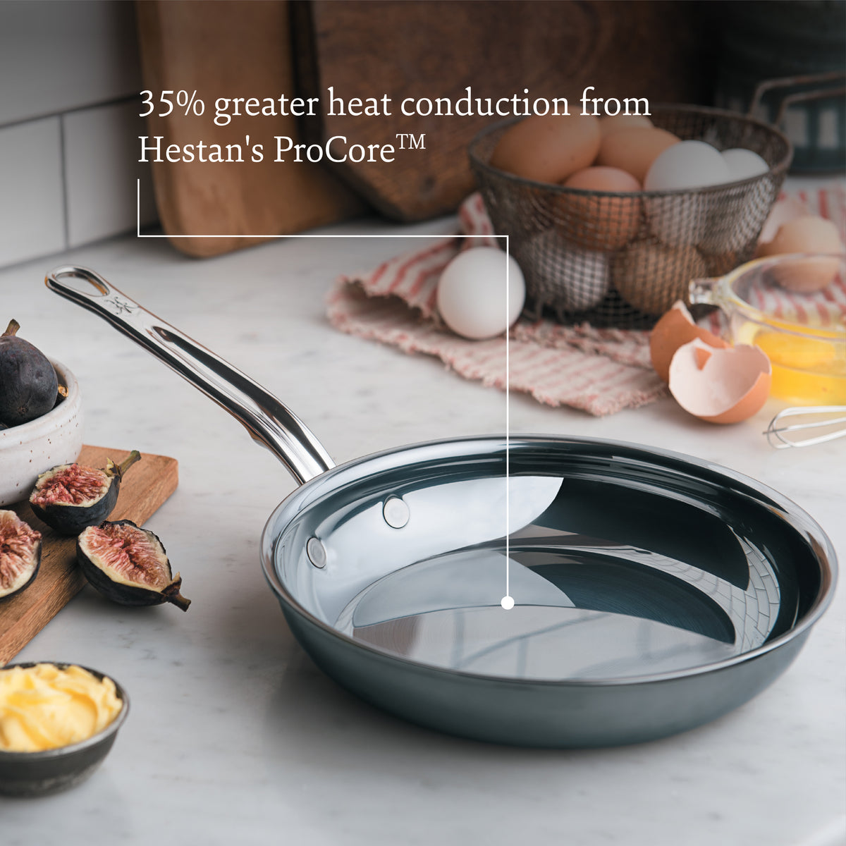 A NanoBond Titanium Induction 4pc Cookware Set with a shiny interior is on a kitchen countertop. Nearby are eggs, butter, figs, and a cloth. Text on the image reads, 35% greater heat conduction from Hestans ProCore™ with Italian handcrafted cookware precision.