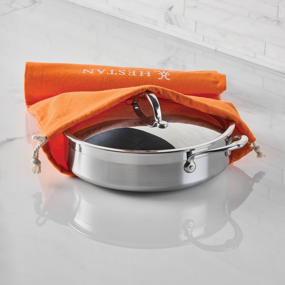 A stainless steel pan with a lid rests on a white marble countertop, partially covered by an Accessories Flannel Cookware Storage Bag—ideal for protecting your cookware.