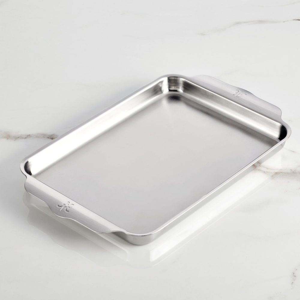 The Hestan OvenBond Tri-Ply Quarter Sheet Pans & Rack, 9-in x 12-in, features raised edges and two handles, elegantly showcased on a white marble surface.