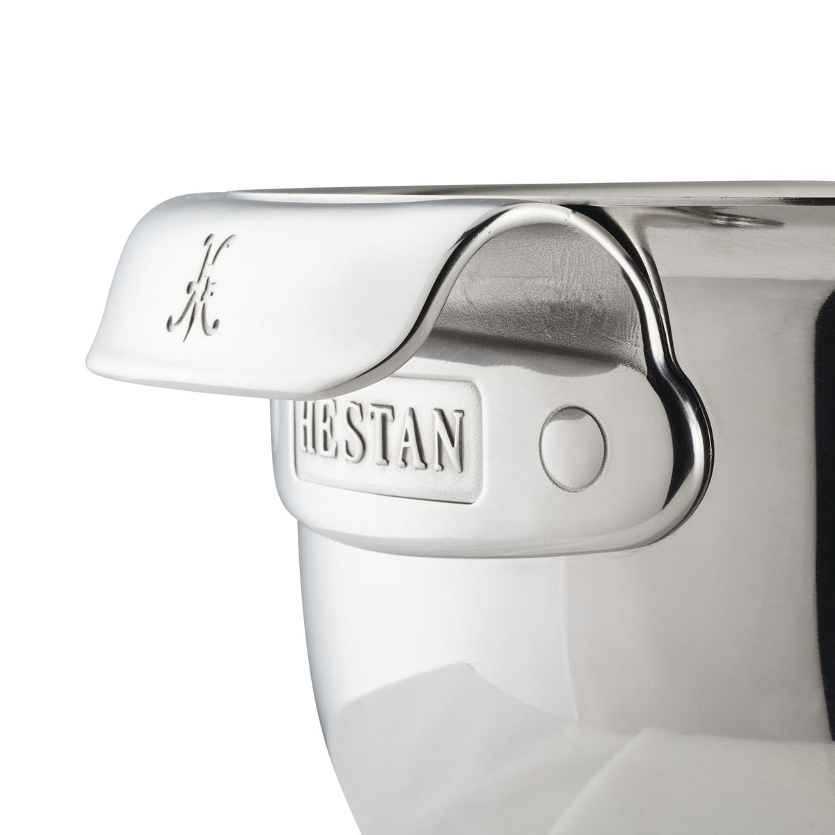 Close-up of a stainless steel mixing bowl with a shiny, reflective surface. The ergonomic handle features an engraved letter H, and Hestan Provisions is embossed beneath it. The heavy-gauge bowls edge curves smoothly, creating a clean and polished appearance.