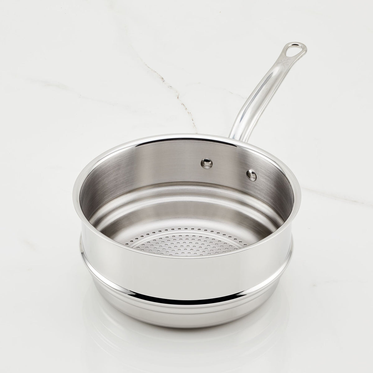 A 3-quart stainless steel pot from Hestan Provisions rests on a white marble surface, boasting a durable steaming insert with a long handle and two rivets. The slightly elevated lid showcases the mesh-like steamer insert inside.