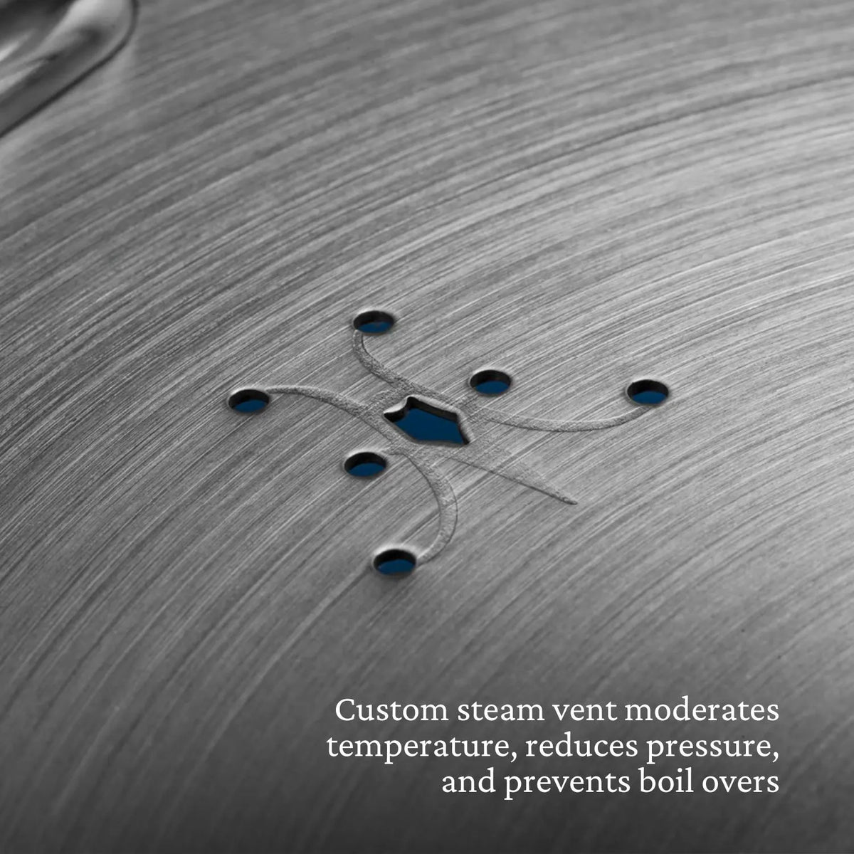 Close-up of brushed metal shows a custom steam vent with small symmetric holes. Text: The Thomas Keller Commercial Clad Stainless Steel 11-Piece Cookware Set features vents that control temperature and prevent boil overs.