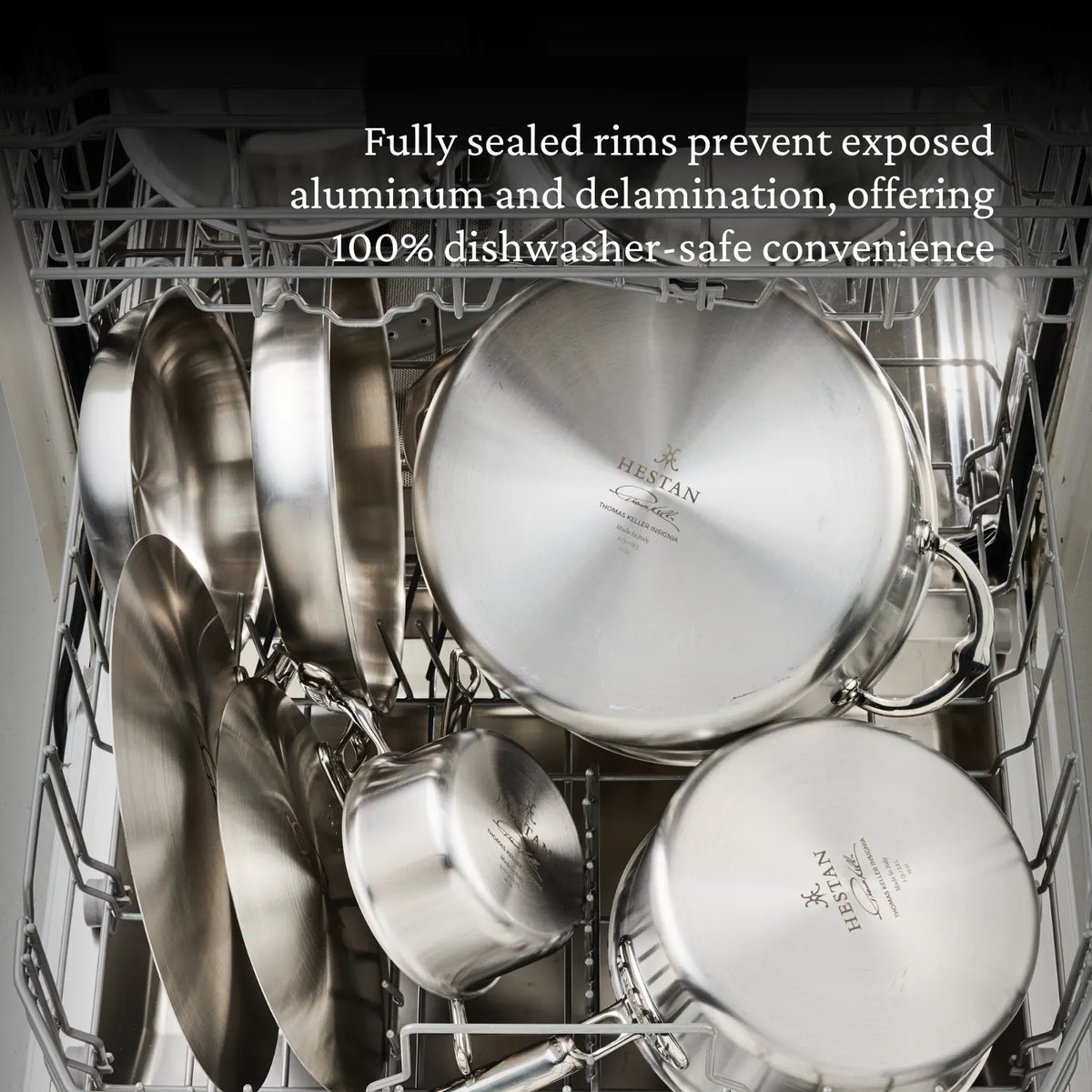 Open dishwasher with Thomas Keller Commercial Clad Stainless Steel 7-Piece Cookware Set, including pots, pans, and lids, loaded in both racks. Top text highlights fully sealed rims for no exposed aluminum and dishwasher safety.
