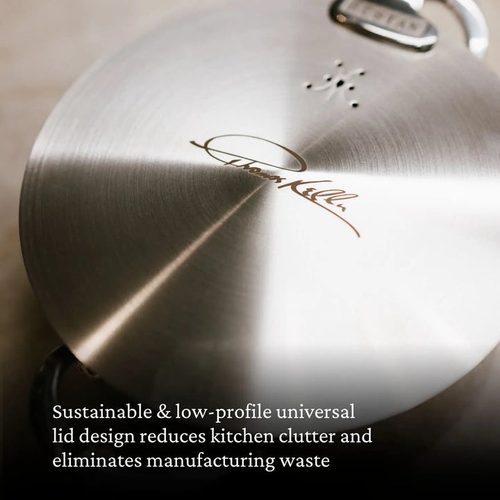 Close-up of a brushed stainless steel pot lid from the Thomas Keller Commercial Clad Stainless Steel 7-Piece Cookware Set, signature engraved, on a gray surface. Text overlay notes its sustainable, low-profile universal design for pro performance.