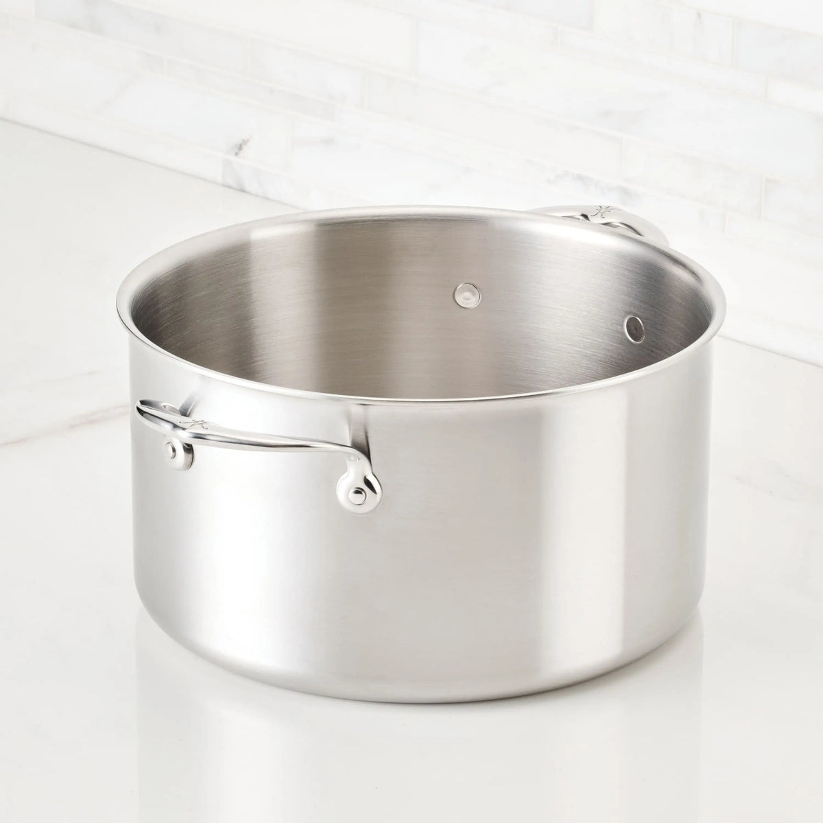 The Thomas Keller Commercial Clad Stainless Steel Stock Pot features a tri-ply construction, two metal handles, and a smooth, brushed finish for professional results—ideal for any kitchen countertop.